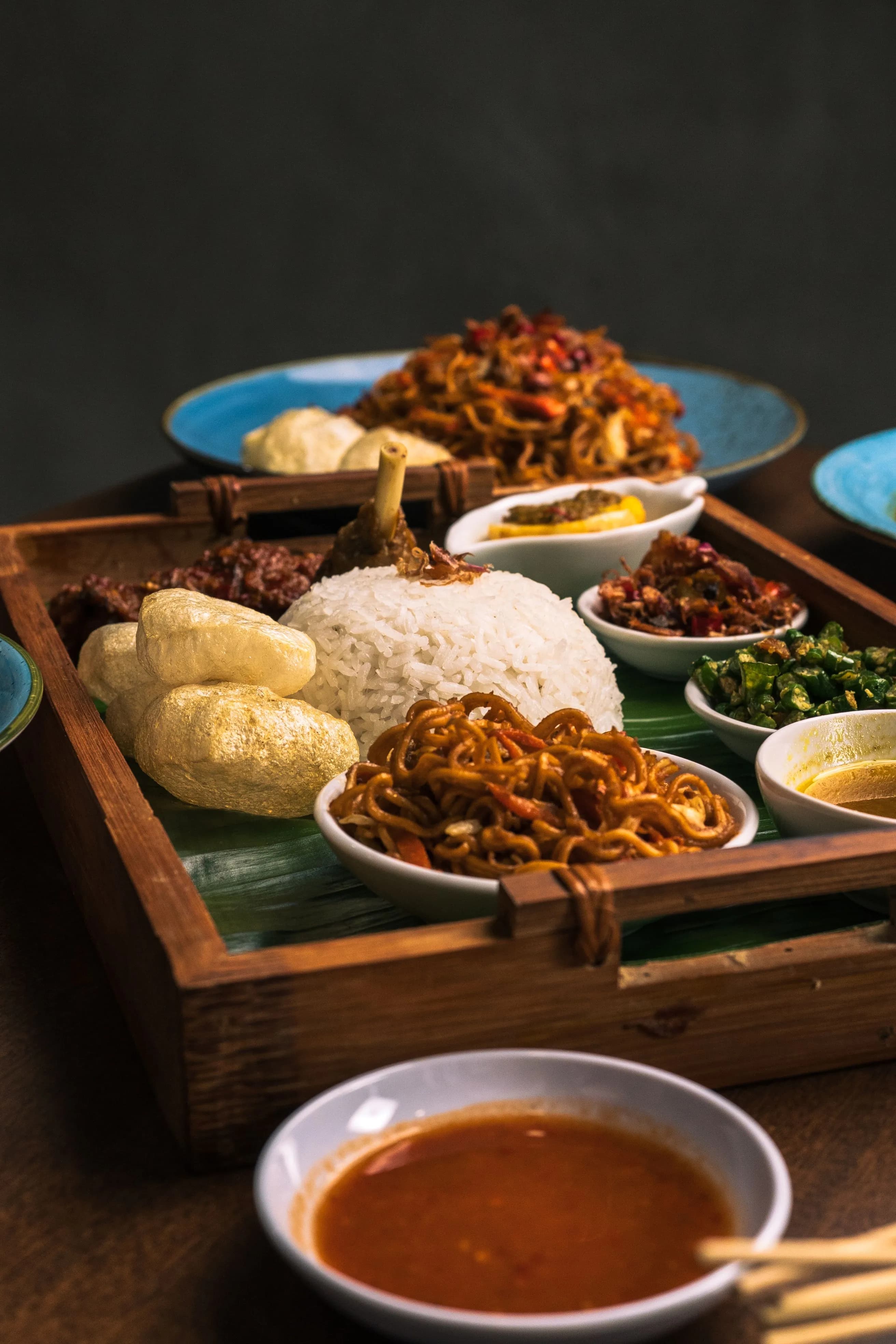 Vibrant Indonesian meal with rice, noodles, and various side dishes in wooden tray