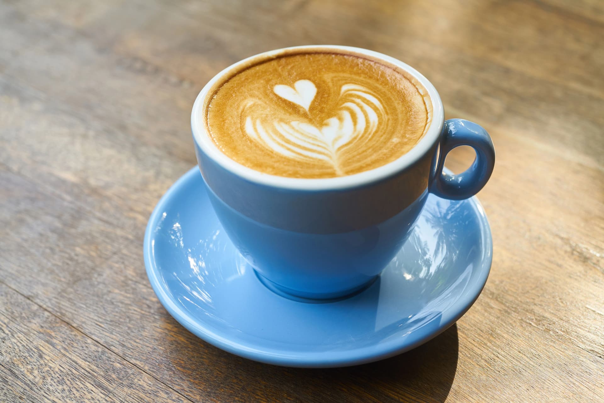 Beautifully crafted latte with heart-shaped art in blue cup on wooden table